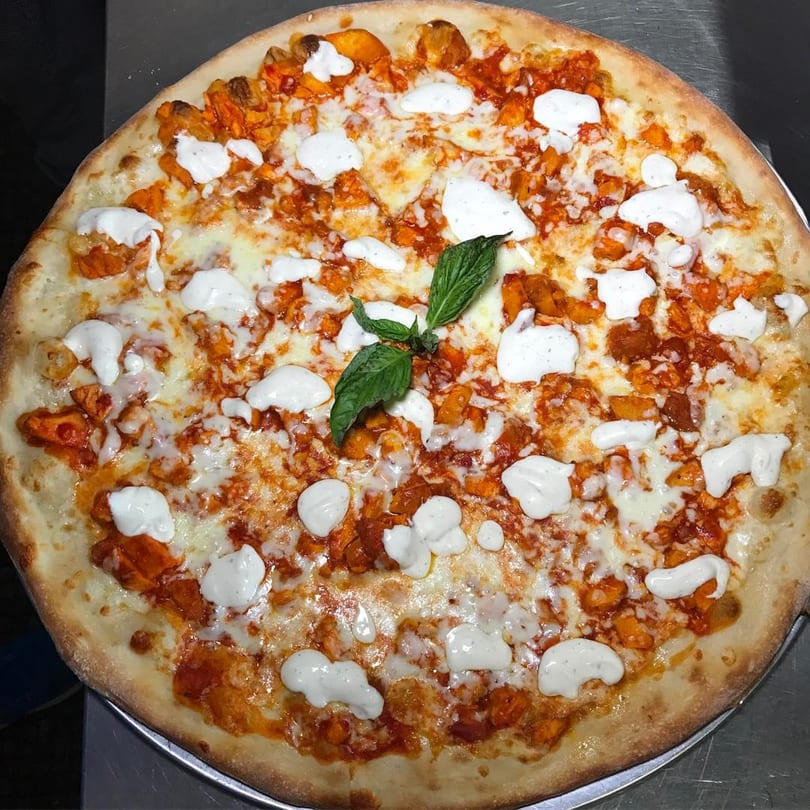 A Surf City Italian Restaurant buffalo chicken pizza with ranch dressing and a basil garnish.