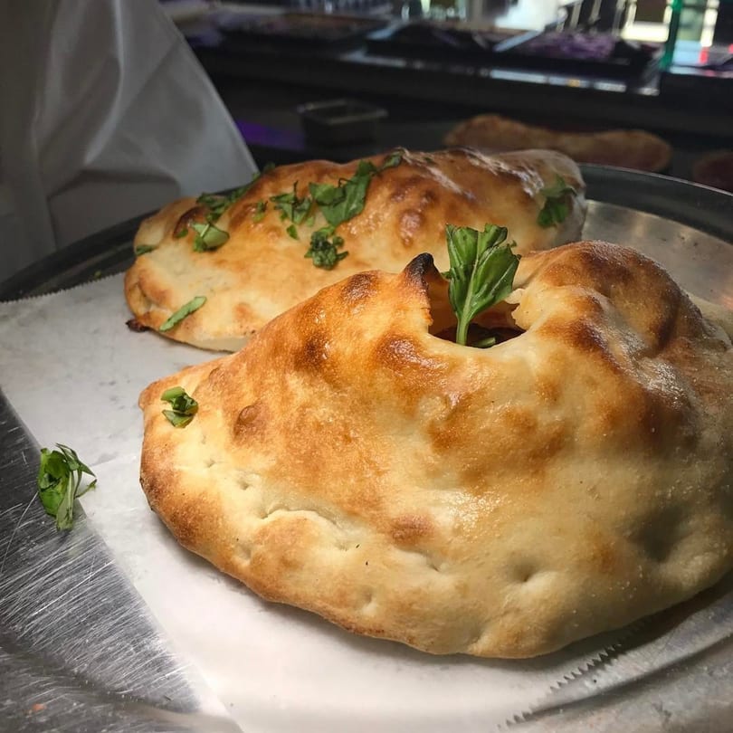 Two golden-brown calzones, one garnished with fresh basil, on a metal tray with parchment paper.