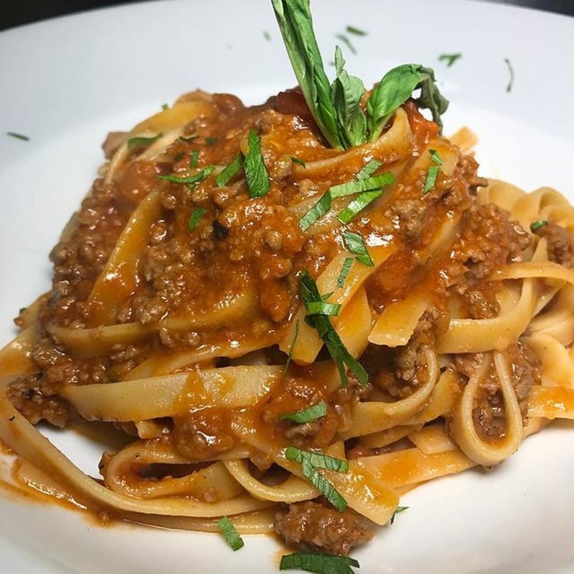 Fettuccine pasta with rich bolognese sauce, garnished with fresh basil on a white plate.