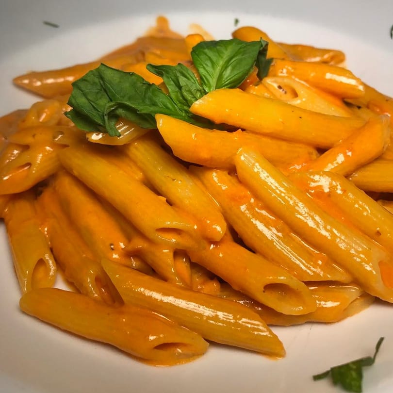 Penne pasta in a creamy orange sauce, garnished with fresh green basil leaves on a white plate.